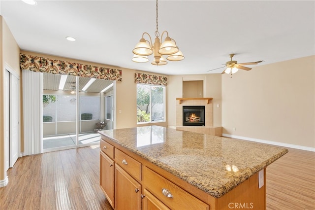 kitchen with light hardwood / wood-style flooring, light stone counters, a center island, pendant lighting, and a fireplace