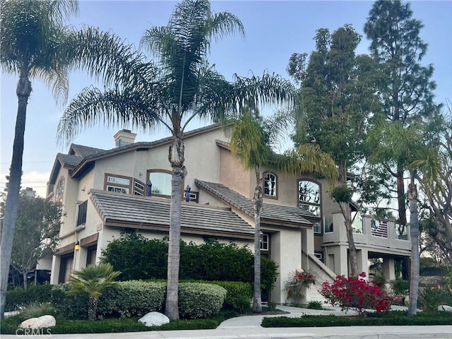 view of front of house with stucco siding, an attached garage, a chimney, and a tiled roof