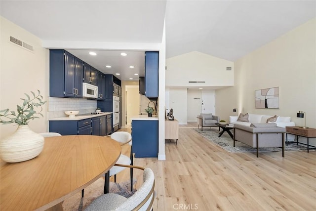 kitchen with white appliances, high vaulted ceiling, tasteful backsplash, blue cabinets, and light wood-type flooring