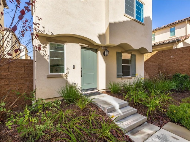 doorway to property featuring fence and stucco siding