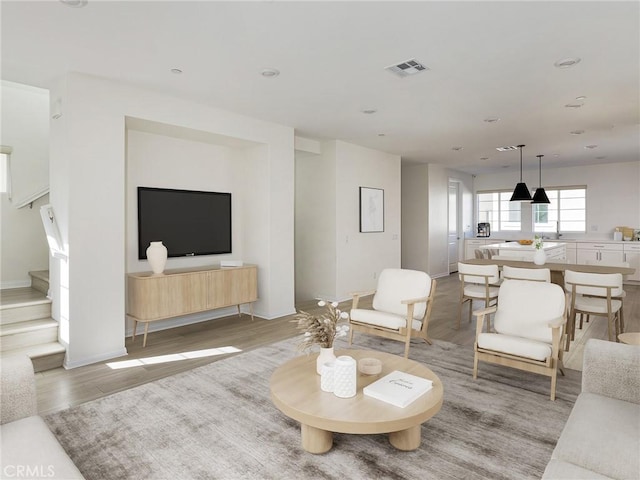 living area with baseboards, light wood-type flooring, stairs, and visible vents
