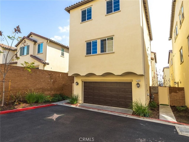 mediterranean / spanish house featuring fence, stucco siding, an attached garage, and aphalt driveway