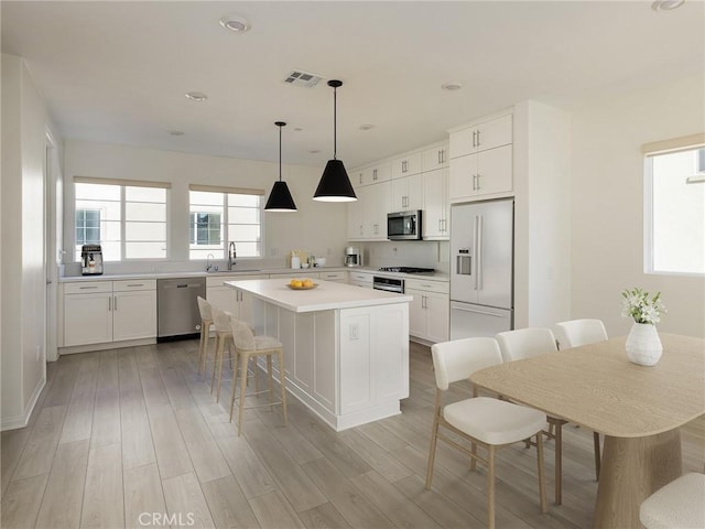 kitchen featuring visible vents, appliances with stainless steel finishes, a center island, a sink, and white cabinets