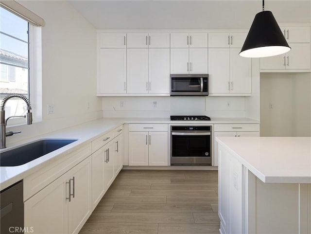kitchen featuring light wood-type flooring, light countertops, white cabinets, a sink, and stainless steel appliances