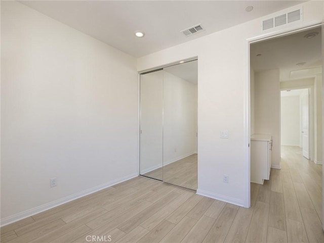 unfurnished bedroom with baseboards, a closet, light wood-type flooring, and visible vents