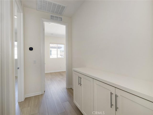 hallway with baseboards, visible vents, and light wood finished floors