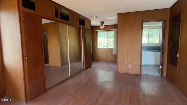 unfurnished bedroom with a closet, hardwood / wood-style flooring, wooden walls, and connected bathroom