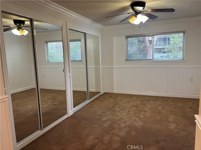 unfurnished bedroom featuring multiple closets, ceiling fan, crown molding, and dark colored carpet