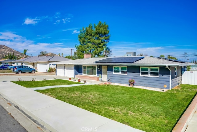 single story home featuring a chimney, an attached garage, roof mounted solar panels, driveway, and a front lawn