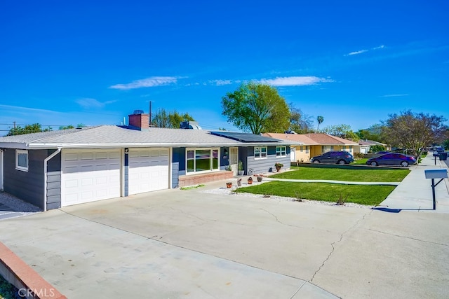 ranch-style home featuring a chimney, concrete driveway, a front yard, roof mounted solar panels, and a garage