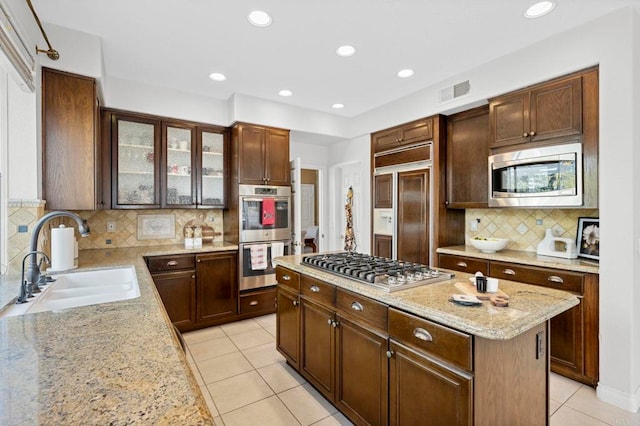 kitchen featuring sink, a center island, built in appliances, light tile patterned floors, and light stone counters