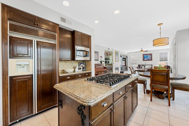 kitchen with a kitchen island, decorative light fixtures, backsplash, built in appliances, and light tile patterned floors