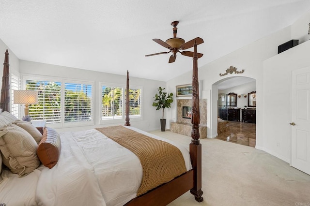 bedroom with ceiling fan, lofted ceiling, a fireplace, and light carpet