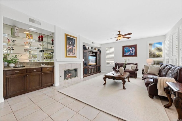 living room featuring ceiling fan, a tile fireplace, and light tile patterned floors