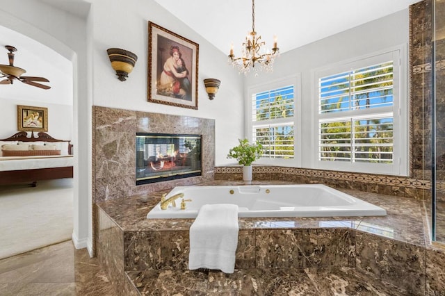 bathroom with a relaxing tiled tub, ceiling fan with notable chandelier, and vaulted ceiling