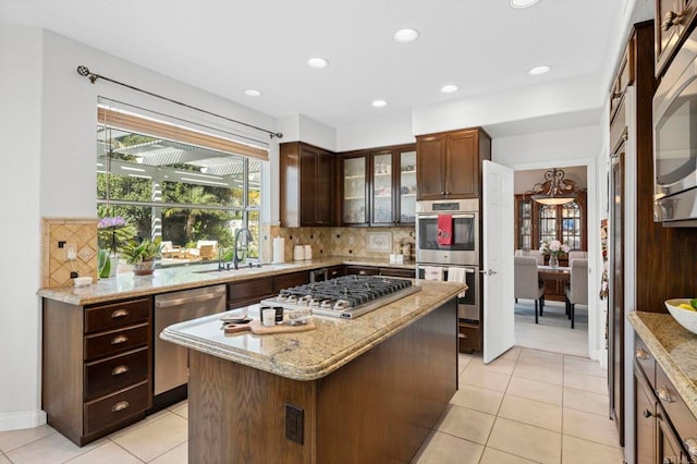 kitchen with appliances with stainless steel finishes, tasteful backsplash, sink, a center island, and light stone counters