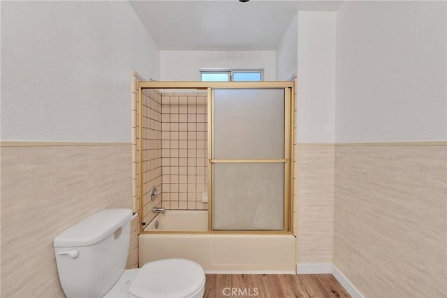 bathroom with hardwood / wood-style flooring, toilet, tile walls, and combined bath / shower with glass door