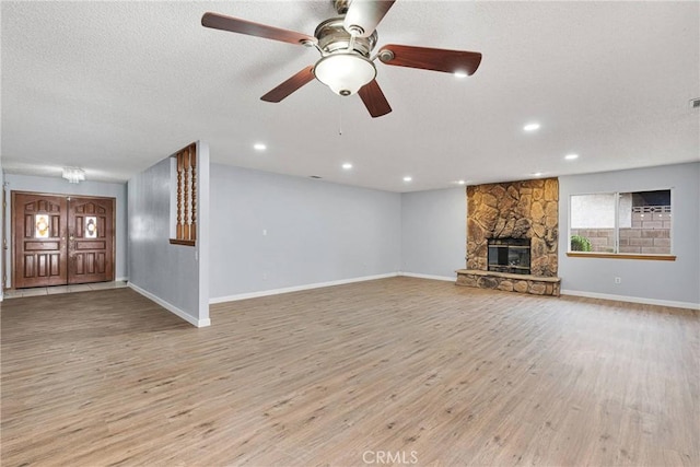 unfurnished living room featuring a fireplace, ceiling fan, light hardwood / wood-style floors, and a textured ceiling