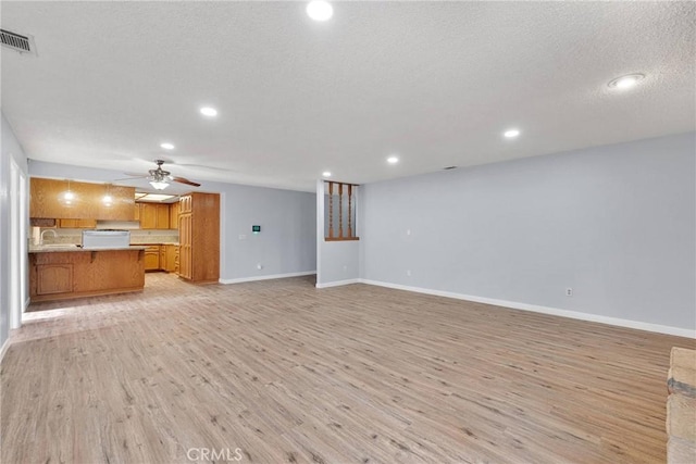 unfurnished living room featuring light hardwood / wood-style floors, ceiling fan, a textured ceiling, and sink