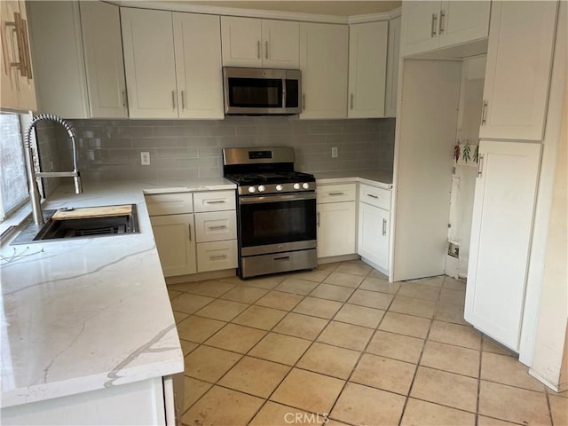 kitchen with appliances with stainless steel finishes, white cabinetry, sink, decorative backsplash, and light stone countertops