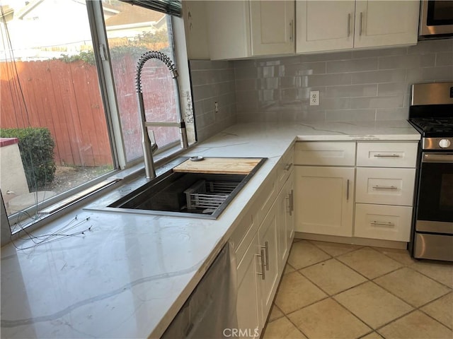 kitchen with sink, white cabinets, decorative backsplash, plenty of natural light, and stainless steel range with gas stovetop