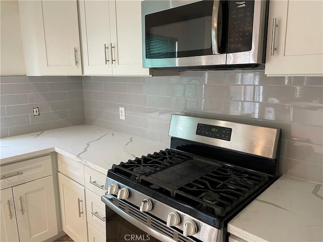 kitchen with tasteful backsplash, white cabinetry, appliances with stainless steel finishes, and light stone counters