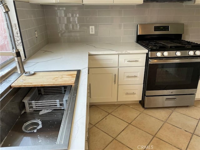 kitchen featuring light tile patterned flooring, stainless steel gas range, white cabinetry, light stone countertops, and backsplash