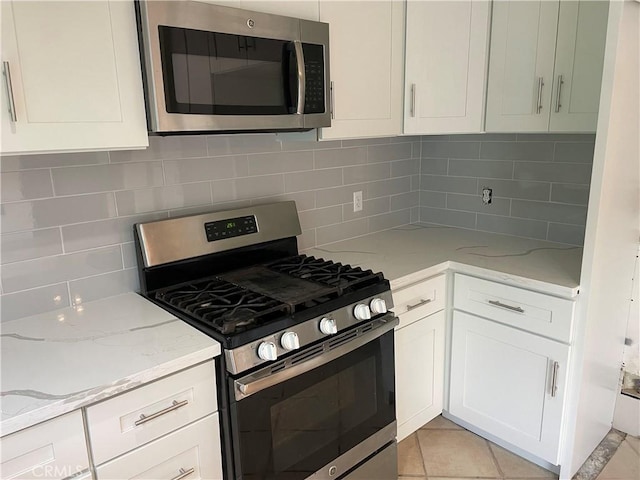 kitchen with appliances with stainless steel finishes, tasteful backsplash, white cabinetry, light tile patterned floors, and light stone countertops