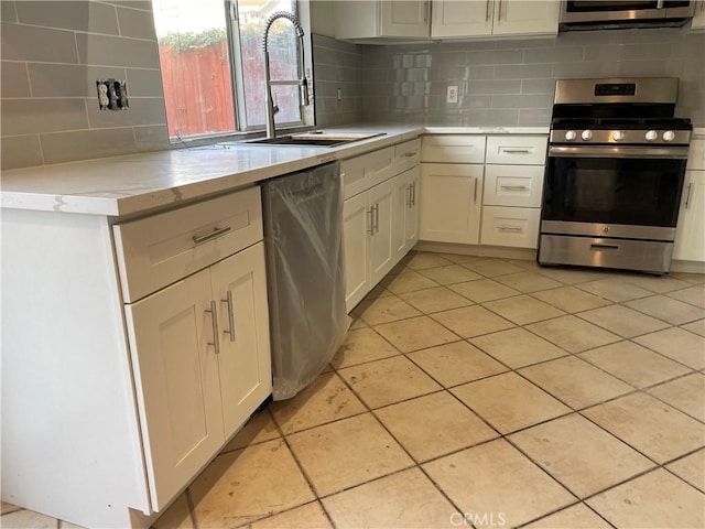 kitchen with light tile patterned flooring, sink, white cabinetry, appliances with stainless steel finishes, and decorative backsplash