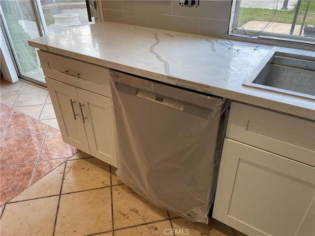 kitchen with dishwasher, white cabinets, decorative backsplash, light tile patterned floors, and light stone counters