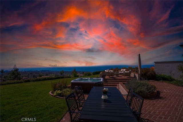 patio terrace at dusk with a yard, outdoor dining area, and a hot tub