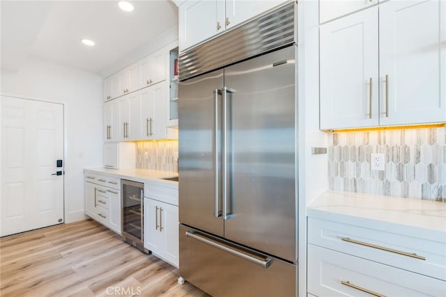 kitchen featuring built in fridge, light stone counters, tasteful backsplash, white cabinetry, and beverage cooler