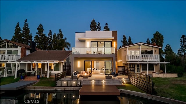 back house at twilight featuring an outdoor hangout area, a patio, a balcony, and a lawn