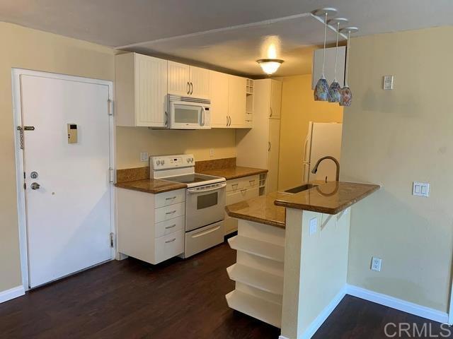 kitchen with sink, white appliances, white cabinets, dark hardwood / wood-style flooring, and kitchen peninsula