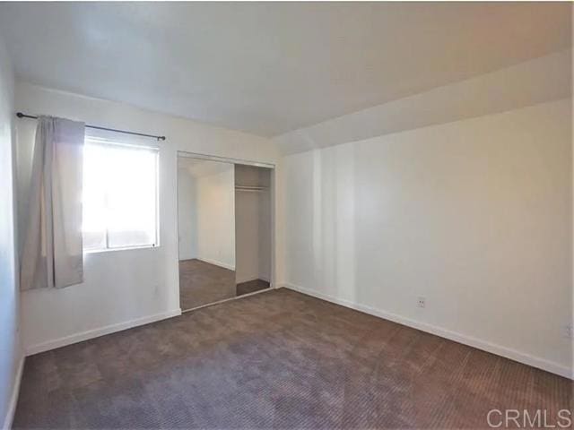 unfurnished bedroom with dark carpet and a closet