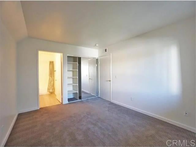 unfurnished bedroom with ensuite bath, a closet, and dark colored carpet