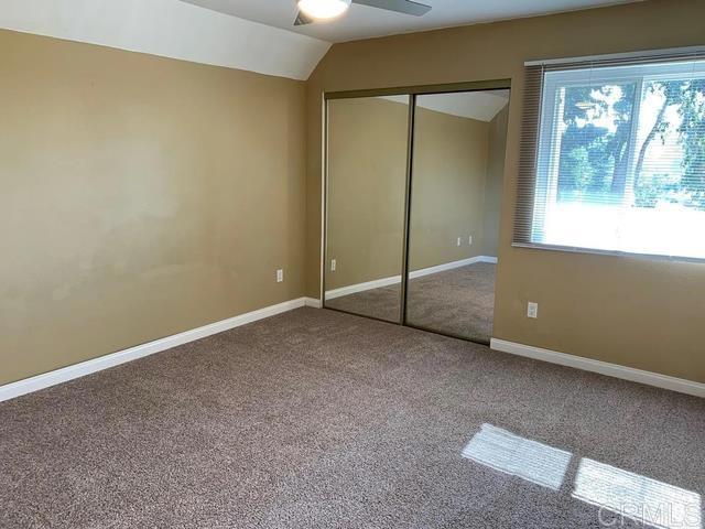 unfurnished bedroom featuring lofted ceiling, carpet flooring, ceiling fan, and a closet