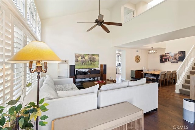 living area featuring ceiling fan with notable chandelier, high vaulted ceiling, dark wood-type flooring, and stairway