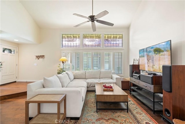 living area with ceiling fan, wood finished floors, a towering ceiling, and baseboards