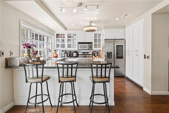 kitchen featuring a peninsula, a sink, visible vents, appliances with stainless steel finishes, and glass insert cabinets