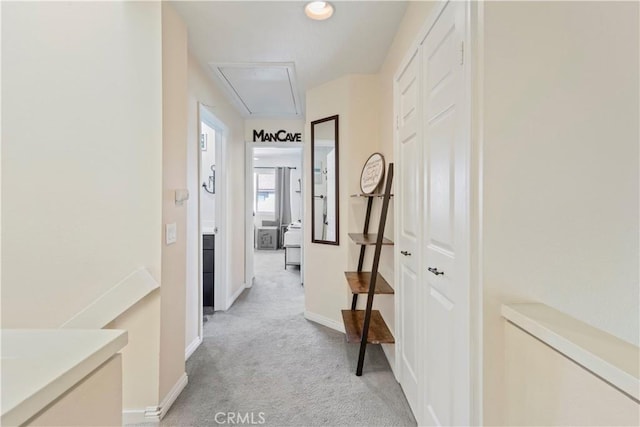 corridor with baseboards, attic access, and light colored carpet