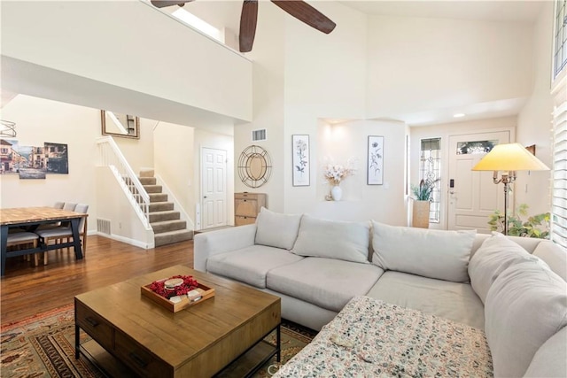 living room with wood finished floors, a towering ceiling, visible vents, stairs, and baseboards