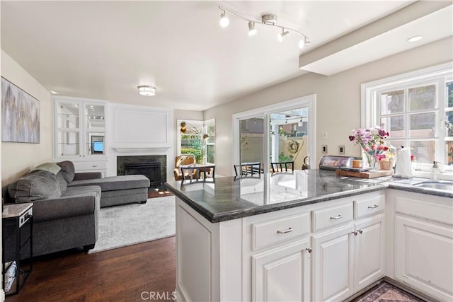 kitchen with dark wood-style flooring, a high end fireplace, white cabinets, dark stone counters, and a peninsula