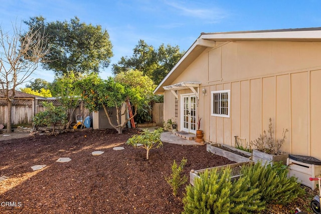 view of yard featuring a garden, french doors, a fenced backyard, and an outdoor structure