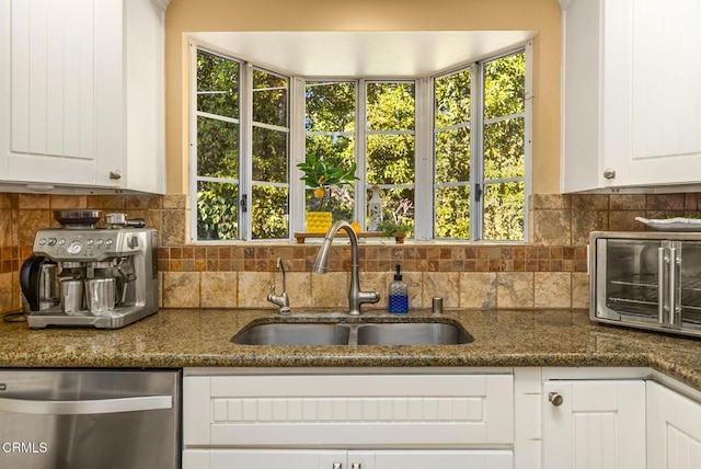 kitchen with a sink, white cabinetry, stainless steel dishwasher, backsplash, and dark stone counters