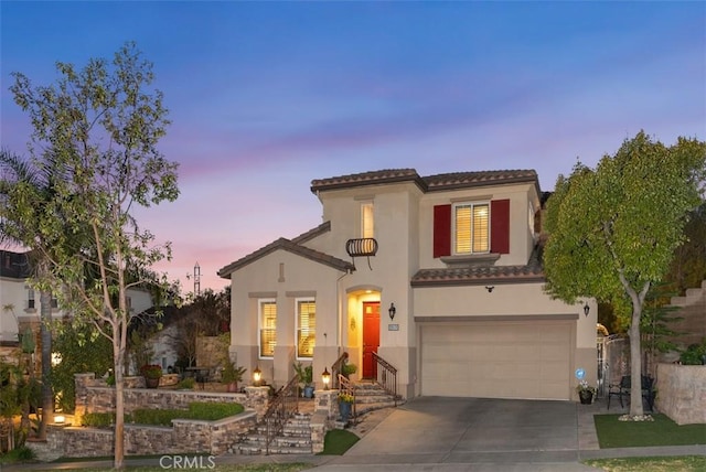 mediterranean / spanish house featuring stucco siding, a garage, driveway, and a tiled roof