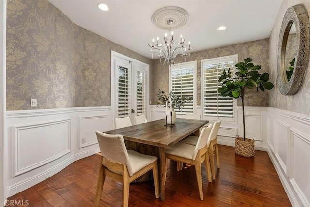 dining area with a chandelier, wainscoting, wallpapered walls, and dark wood-style flooring