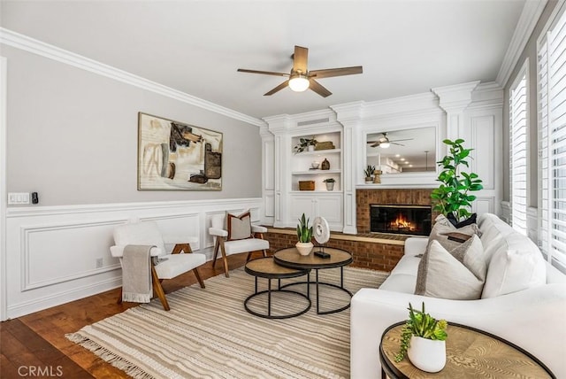 sitting room featuring wood finished floors, a wainscoted wall, ceiling fan, crown molding, and a brick fireplace