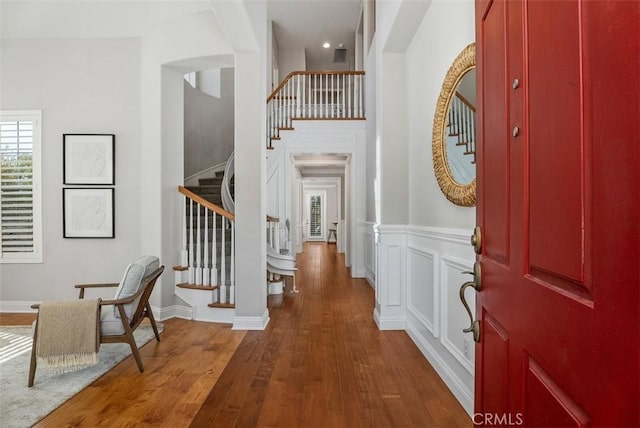 entryway with a decorative wall, a wainscoted wall, stairs, and wood finished floors