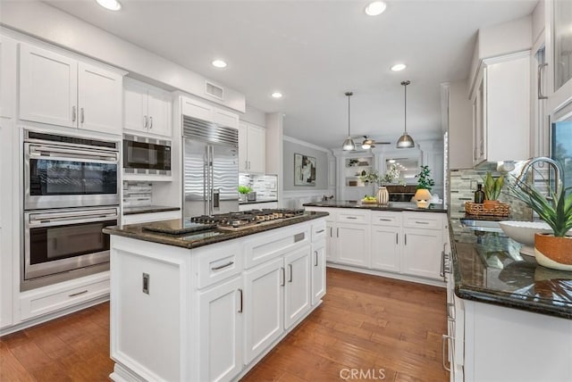 kitchen featuring a peninsula, backsplash, wood finished floors, and built in appliances